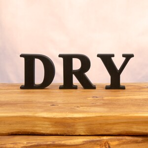 May include: The word "DRY" spelled out in black block letters on a wooden surface.