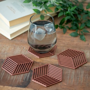 May include: Four brown geometric coasters with a glass of iced water on one of them. The coasters are made of a textured material and have a 3D effect.