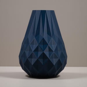 May include: A dark blue geometric vase with a textured surface. The vase is sitting on a wooden table with three round candle holders.