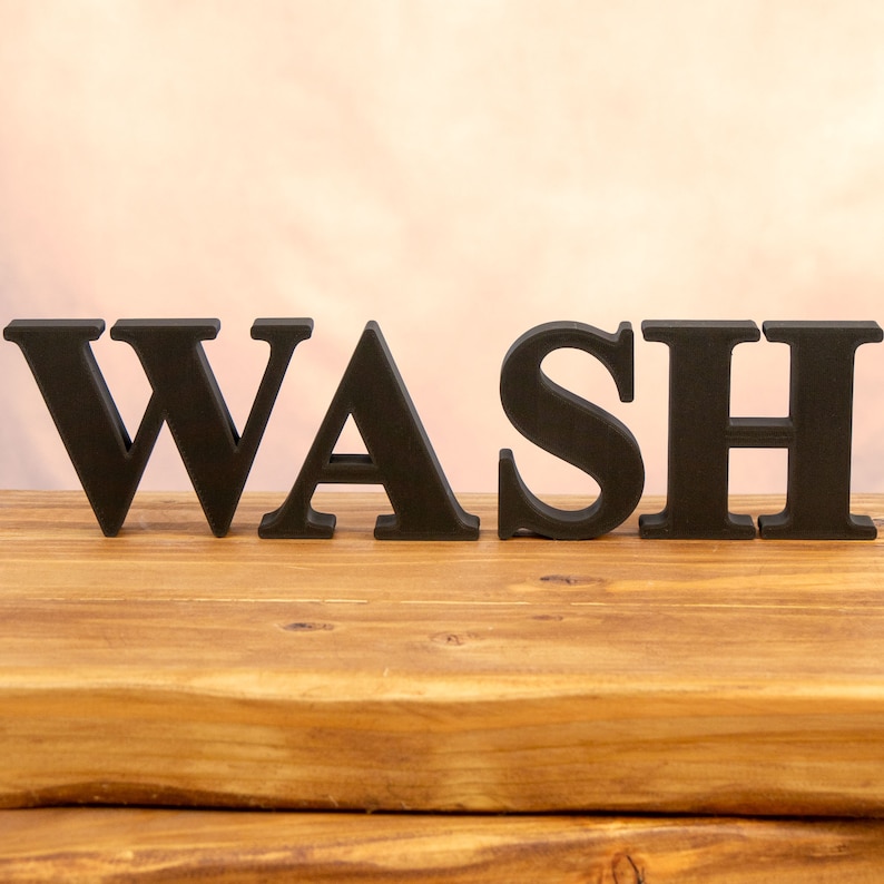 May include: Black wooden letters spelling out the word "WASH" on a wooden surface.