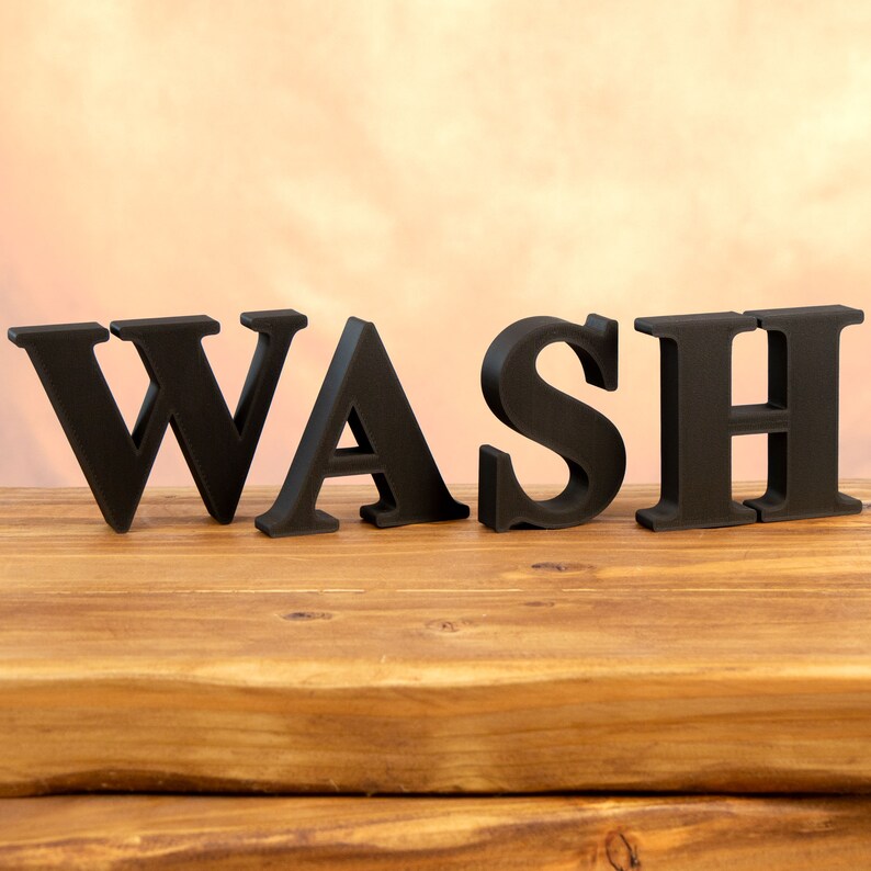 May include: Black wooden letters spelling out the word "WASH" on a wooden surface.