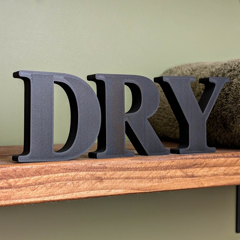 May include: Black wooden letters spelling "DRY" on a wooden shelf.
