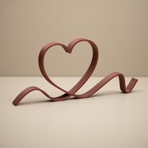 May include: A mauve heart-shaped sculpture with a flowing ribbon design. The sculpture is made of a solid material and sits on a neutral surface. The heart shape is clearly defined, and the ribbon adds a sense of movement.