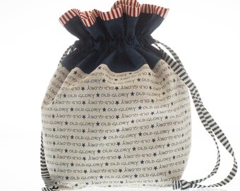 May include: A white drawstring bag with a blue denim top and red and white striped trim. The bag is printed with the words "Old Glory" repeated many times.