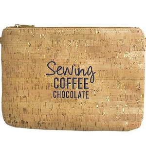 May include: A rectangular cork clutch with a gold zipper and strap. The bag has gold flecks and the words "Sewing, Coffee, Chocolate" in navy blue. A matching strap is attached.