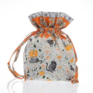 May include: A white drawstring bag with a black and orange print of cats, pumpkins, and flowers. The bag has a bright orange lining and is perfect for Halloween treats.