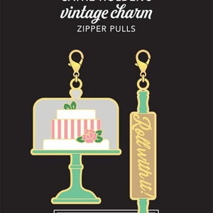 May include: Two gold zipper pulls with a vintage charm theme. One pull features a pink and white cake under a glass dome. The other pull features a rolling pin with the text "Roll with it!" in gold lettering.