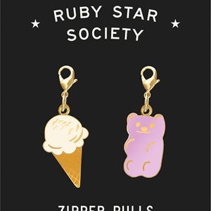 May include: Two gold zipper pulls with charms. One charm is a pink gummy bear and the other is a white ice cream cone on a waffle cone. The text "RUBY STAR SOCIETY" is at the top of the image and the text "ZIPPER PULLS by Kimberly Kight" is at the bottom.
