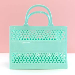 May include: A light green plastic tote bag with two arched handles. The bag features a rectangular shape with a lattice design on the front and back. The bag is made of a solid, smooth plastic material.