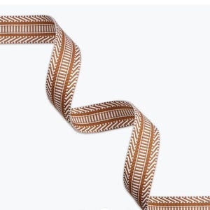 May include: A woven fabric ribbon featuring a repeating pattern of vertical white lines centered between two rows of diagonal white chevron stripes on a solid brown background. The ribbon is displayed in a curved, flowing S-shape configuration.