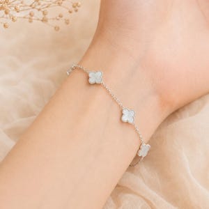 May include: A silver-toned chain bracelet featuring three evenly spaced four-leaf clover charms. Each clover charm is inlaid with a smooth, iridescent white stone and framed by a delicate beaded metal border, connected by a thin, polished link chain.