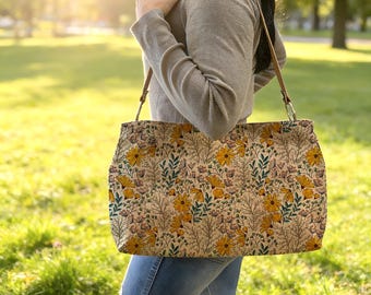 May include: A rectangular shoulder bag featuring a light beige background with a repeating pattern of yellow flowers, green leaves, and thin brown branches. The bag has two thin brown straps attached to the top with silver-toned metal rings.