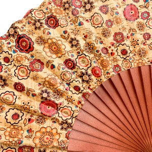 May include: A hand fan with a brown wooden frame and a beige fabric panel with a floral pattern in shades of red, orange, and brown.