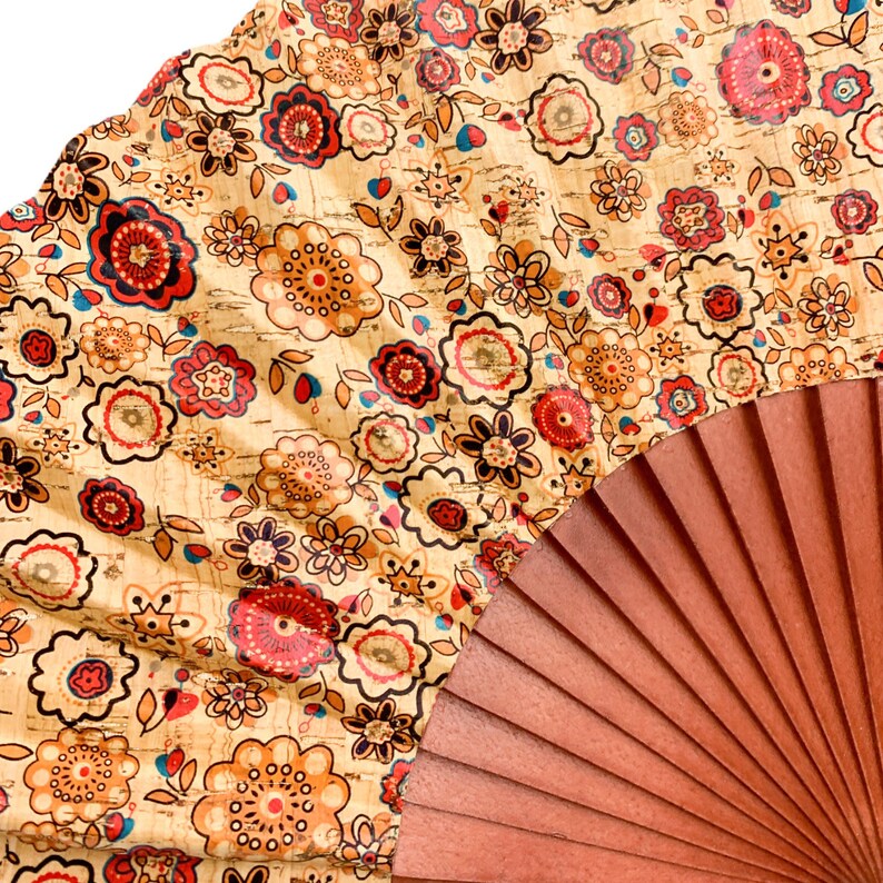 May include: A hand fan with a brown wooden frame and a beige fabric panel with a floral pattern in shades of red, orange, and brown.
