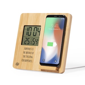 May include: A bamboo charging station with a digital clock and a quote that reads "Happiness is the absence of the striving for happiness." The station has a slot for a smartphone, which is shown charging with a 64% battery level.