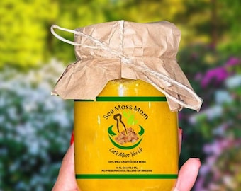 May include: A glass jar with a yellow liquid inside. The jar has a brown paper label with the text "Sea Moss Mom" and "Let's Moss You Up". The label also says "100% Wild Crafted Sea Moss", "16 FL OZ (473.2 ML)", and "No Preservatives, Fillers or Binders".