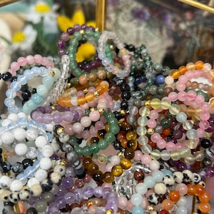 May include: A collection of colorful beaded bracelets made with various gemstones, including amethyst, rose quartz, tiger's eye, and green aventurine.
