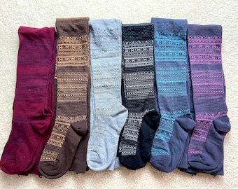 May include: A collection of seven pairs of patterned tights in various colors. The tights feature a repeating geometric design in shades of burgundy, brown, gray, black, blue, and purple. The tights are folded and displayed on a white surface.