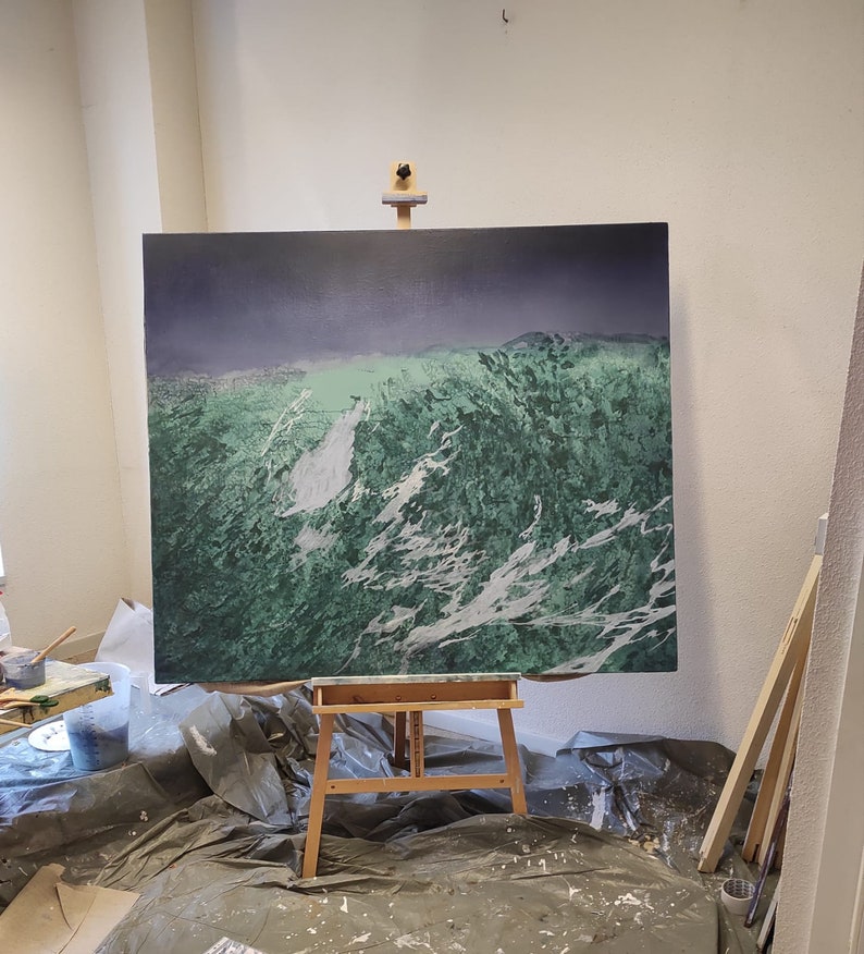 May include: A large canvas painting on an easel in a studio setting. The painting depicts a landscape with green and white brushstrokes, suggesting a mountainous or wave-like scene.
