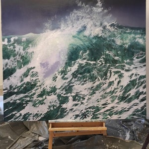 May include: A large painting on canvas depicting a large, crashing ocean wave with white foam and green water. The painting is on an easel in a room with a gray tarp on the floor.