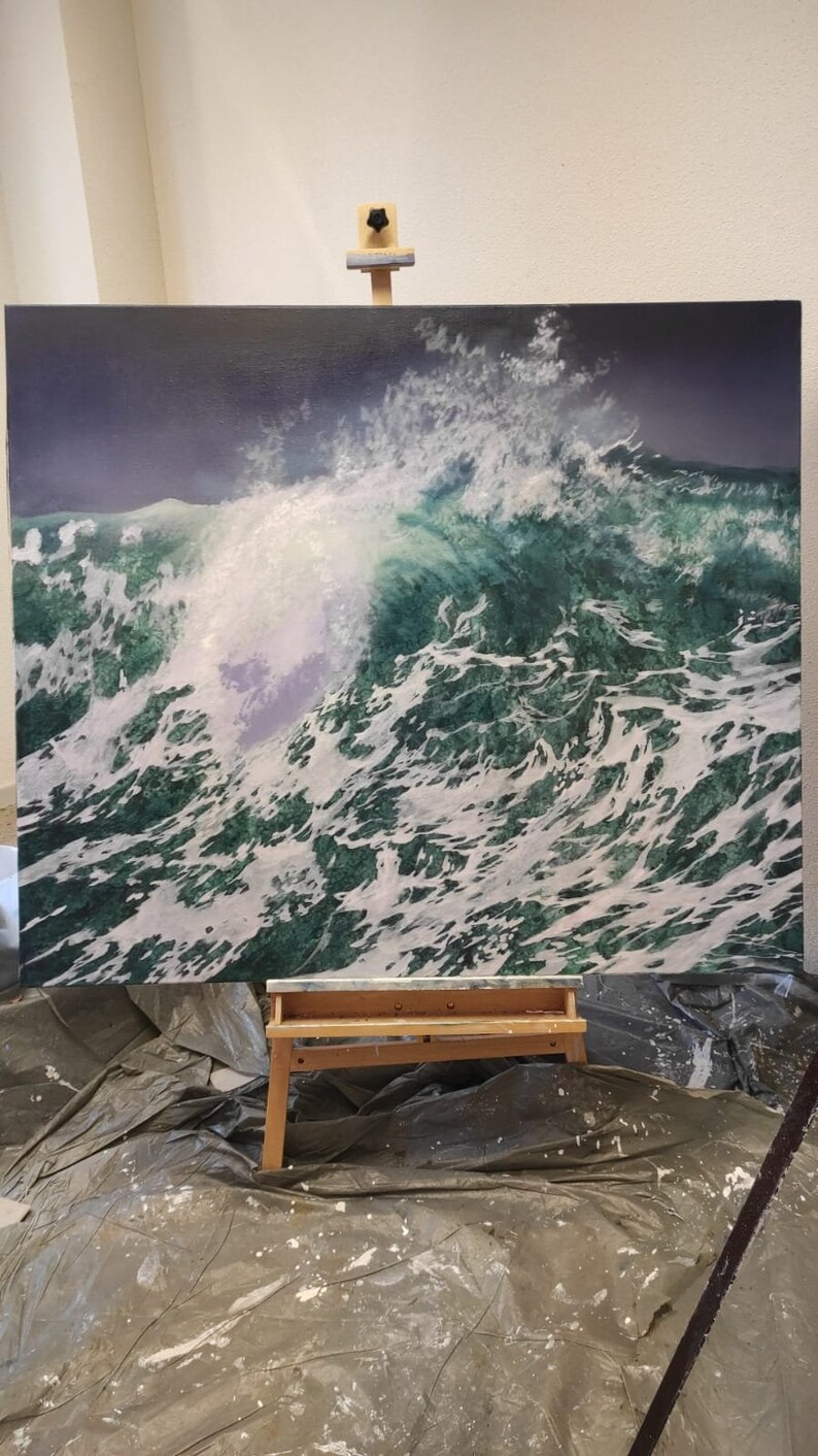 May include: A large painting on canvas depicting a large, crashing ocean wave with white foam and green water. The painting is on an easel in a room with a gray tarp on the floor.