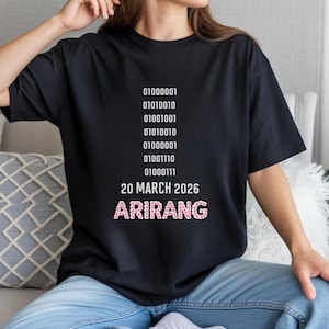 May include: Black t-shirt with white binary code and the text "20 MARCH 2026 ARIRANG" in pink floral letters. The shirt is a casual style, suitable for everyday wear.