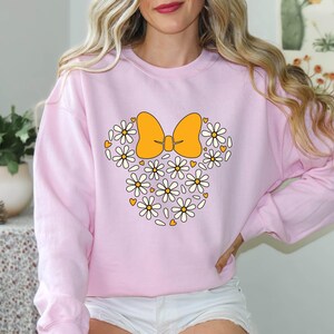 Puede incluir: Sudadera rosa con un dise&ntilde;o floral blanco y amarillo en forma de lazo. El lazo est&aacute; hecho de flores blancas y amarillas.