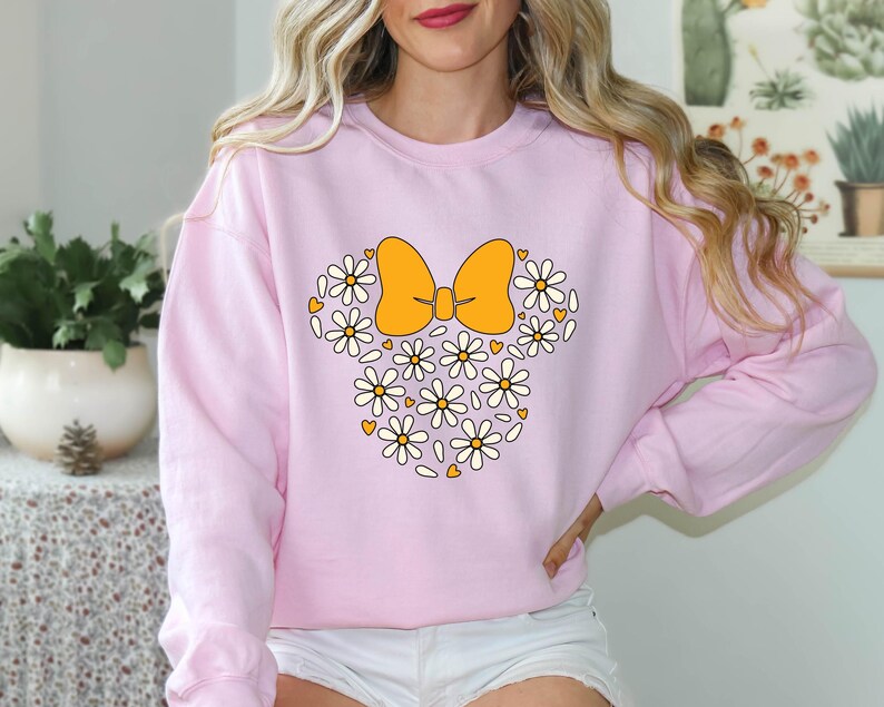 Puede incluir: Sudadera rosa con un dise&ntilde;o floral blanco y amarillo en forma de lazo. El lazo est&aacute; hecho de flores blancas y amarillas.