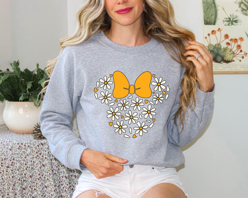 Puede incluir: Una sudadera gris con un dise&ntilde;o floral con un lazo amarillo. El dise&ntilde;o recuerda la cabeza de un personaje de dibujos animados.