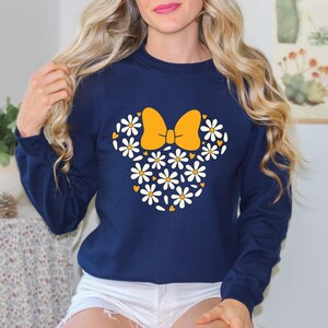 Puede incluir: Una sudadera azul marino con un dise&ntilde;o de margaritas blancas y amarillas en forma de la cabeza de Minnie Mouse.