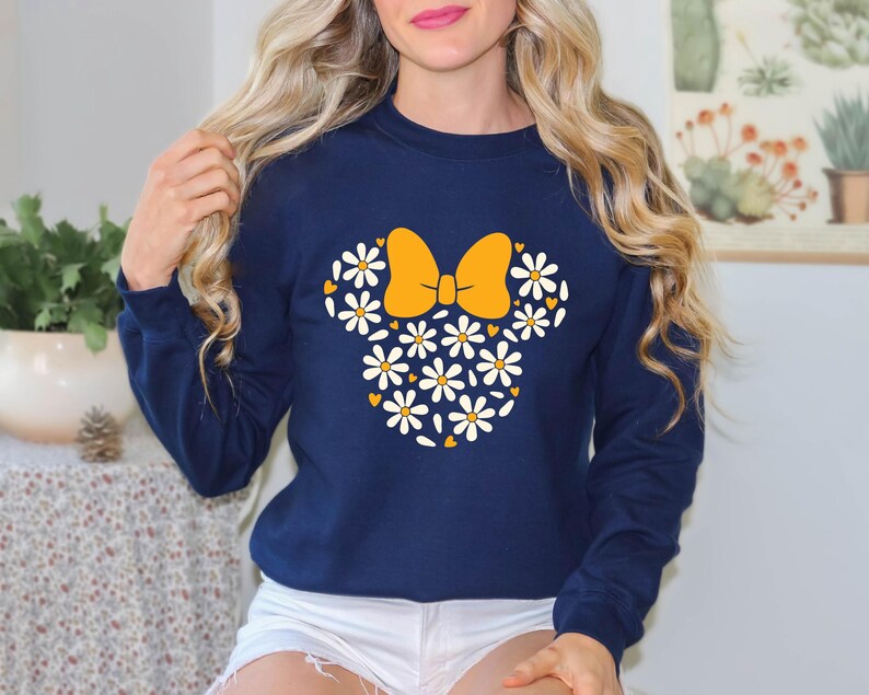 Puede incluir: Una sudadera azul marino con un dise&ntilde;o de margaritas blancas y amarillas en forma de la cabeza de Minnie Mouse.