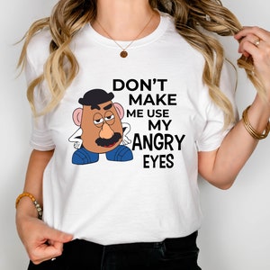 Może przedstawiać: Biała koszulka z kresk&oacute;wkowym wizerunkiem Pana Potato Head z tekstem "Nie zmuszaj mnie do używania moich złych oczu."