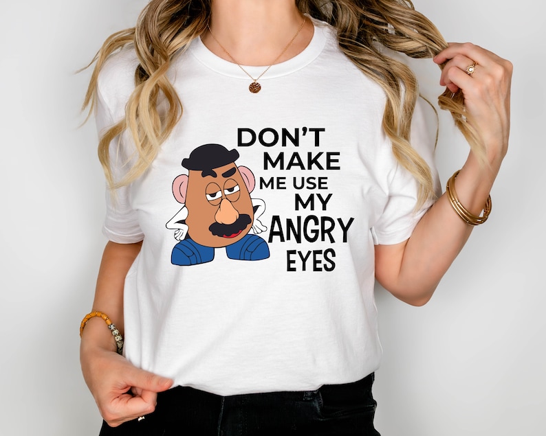 Może przedstawiać: Biała koszulka z kresk&oacute;wkowym wizerunkiem Pana Potato Head z tekstem "Nie zmuszaj mnie do używania moich złych oczu."