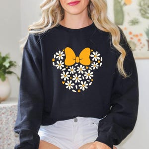 Puede incluir: Sudadera negra con un dise&ntilde;o floral de Minnie Mouse con un lazo amarillo y margaritas blancas.