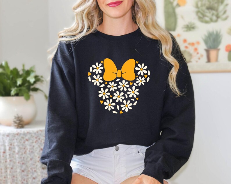 Puede incluir: Sudadera negra con un dise&ntilde;o floral de Minnie Mouse con un lazo amarillo y margaritas blancas.