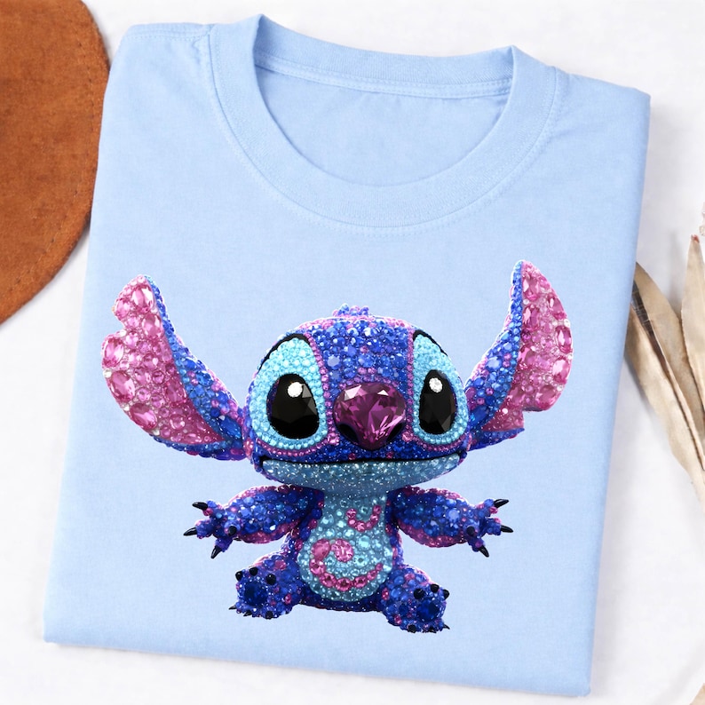 K&ouml;nnte beinhalten: Hellblaues T-Shirt mit einem funkelnden Stitch-Charakterdesign. Die Figur ist haupts&auml;chlich blau mit rosa Akzenten an Ohren und Brust. Das Shirt besteht aus einem weichen Material und ist f&uuml;r den Freizeitgebrauch geeignet.