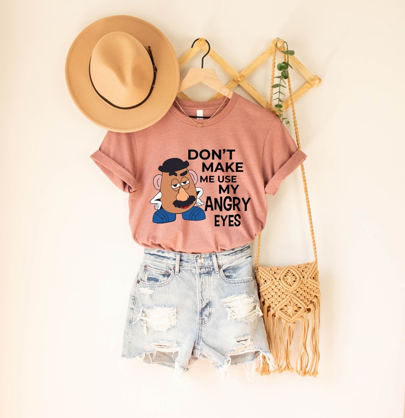 Może przedstawiać: R&oacute;żowa koszulka z grafiką Pana Potato Head z tekstem "Nie zmuszaj mnie do używania moich złych oczu".