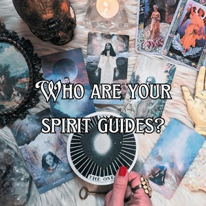 May include: A tarot card reading with the question "Who are your spirit guides?" written in black text on a white background. The cards are spread out on a white fuzzy surface with a crystal, a wooden hand, and a small skull.