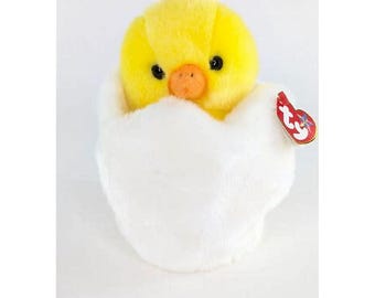 May include: A yellow chick plush toy in a white egg-shaped plush toy. The chick has black eyes and a small orange beak. The egg has a red Ty tag attached to it.