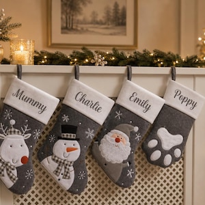 May include: Four grey felt Christmas stockings with white cuffs personalised with the names Mummy, Charlie, Emily, and Poppy. The stockings feature embroidered designs of a reindeer, a snowman, a Santa Claus, and a white paw print.