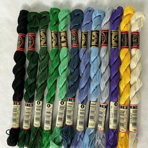 May include: A collection of twelve DMC Coton Perle embroidery thread skeins in various colors including black, green, blue, purple, yellow, and cream. Each skein features a black and gold paper label with the DMC logo and color number.