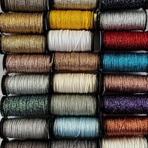May include: A collection of spools of metallic thread in various colors, including gold, silver, red, and blue. The thread is tightly wound on black spools, creating a visually appealing display. Ideal for crafting and embellishment projects.