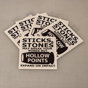 Puede incluir: Un conjunto de seis pegatinas blancas con texto negro y una ilustración en blanco y negro de una bala. El texto en las pegatinas dice "Sticks & Stones May Break Your Bones But Hollow Points Expand On Impact".