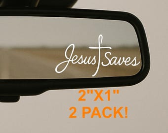 May include: A car rearview mirror with the words "Jesus Saves" in white script and a cross symbol. The text "2"x1" 2 PACK!" is below the text. The background shows a road.