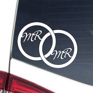 May include: White vinyl decal of two interlocking rings with the word "MR" inside each ring. The decal is on a car window.