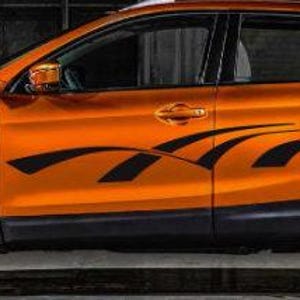May include: An orange SUV with black accents and black wheels. The vehicle has a black graphic design on the side. The car is parked in front of a dark background.