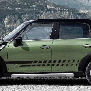 May include: A green Mini Cooper Countryman with black accents, including the roof, wheels, and fender flares. Black graphic decals run along the side. The car is parked on a gravel surface with a mountain and water backdrop.