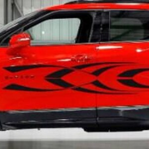 May include: A red SUV with black accents and black wheels. The vehicle has a decorative black tribal design on the side. The car is parked indoors.