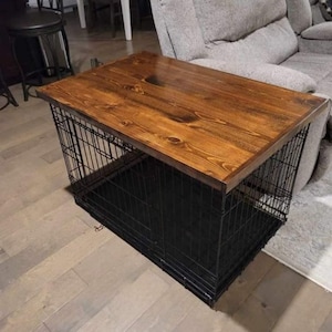 May include: A black metal dog crate with a wooden top. The crate is sitting on a wooden floor. The wooden top is stained a dark brown color.