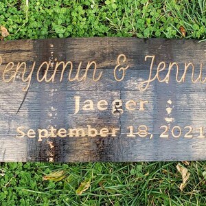 May include: A dark brown wooden sign with metal accents and the text "Benjamin & Jennifer Jaeger September 18, 2021" engraved in gold.